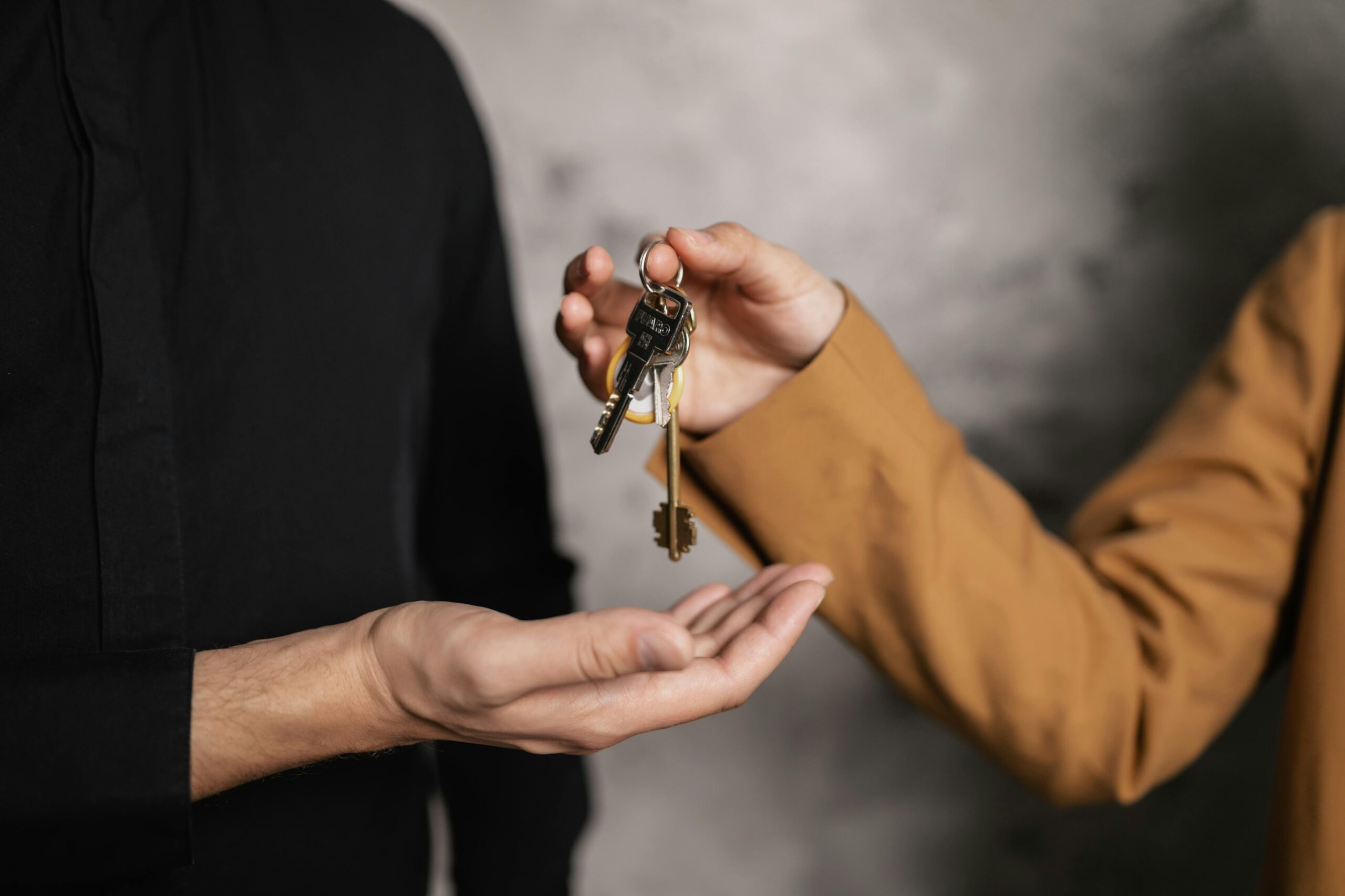 Detailed close-up of one person handing over keys to another, symbolizing a real estate transaction.